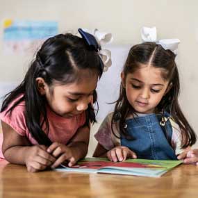 Two young girls looking at a colorful book